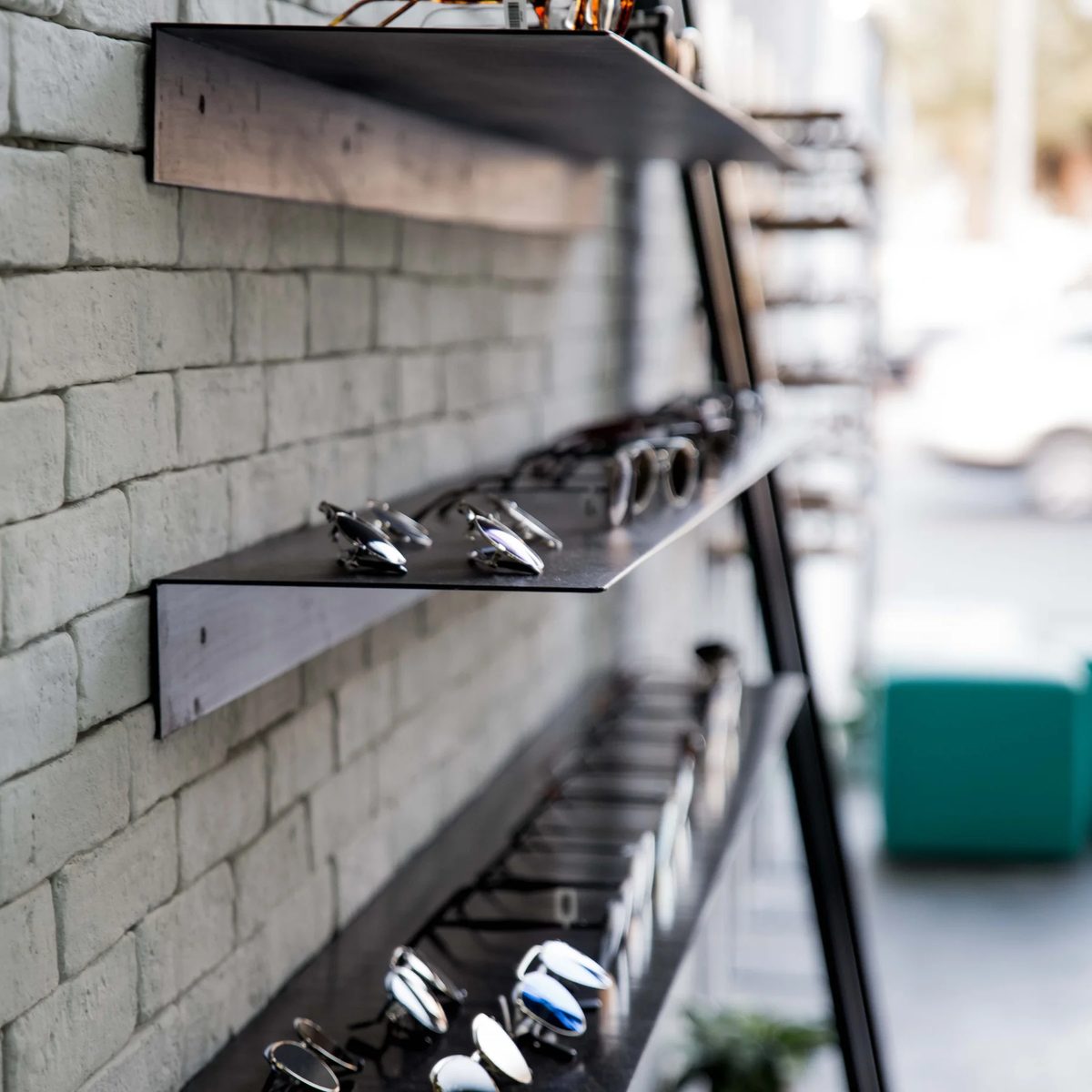 Close view of angled metal eyewear display shelf against white block wall in Jamjom prototype