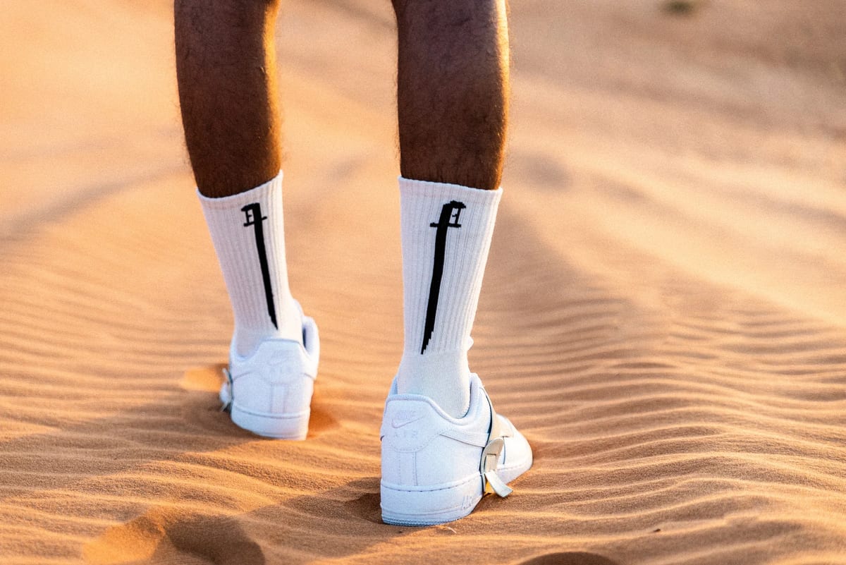 White Nike desert footwear seen from behind on rippled Saudi sand at sunset