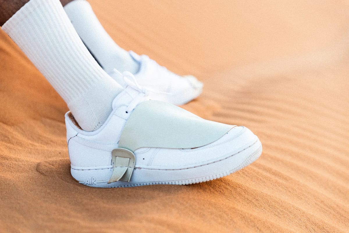 Side close-up of white Nike desert footwear pressing into warm sand