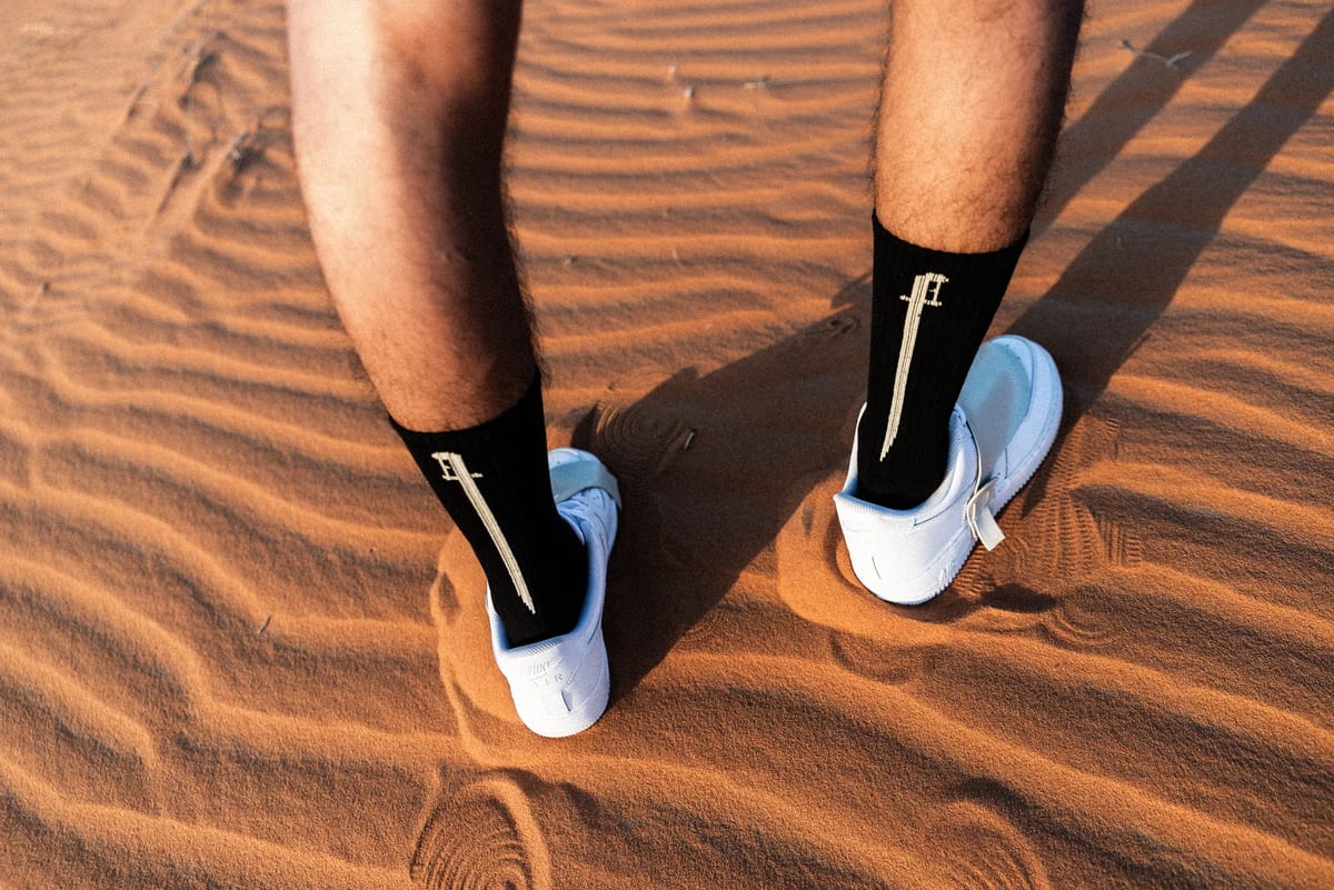 Black and white Nike socks with white shoes leaving tracks across rippled desert sand